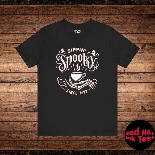 Charming Halloween design featuring a skeleton hand holding a coffee cup with the phrase "Sippin' Spooky Since 1692." Perfect for coffee lovers who enjoy a spooky twist during the Halloween season.